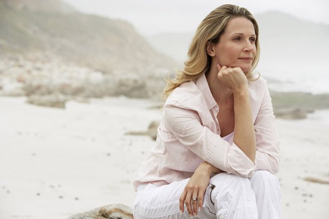 Blonde Frau sitz frei von Sorgen am Strand und genießt die Aussicht